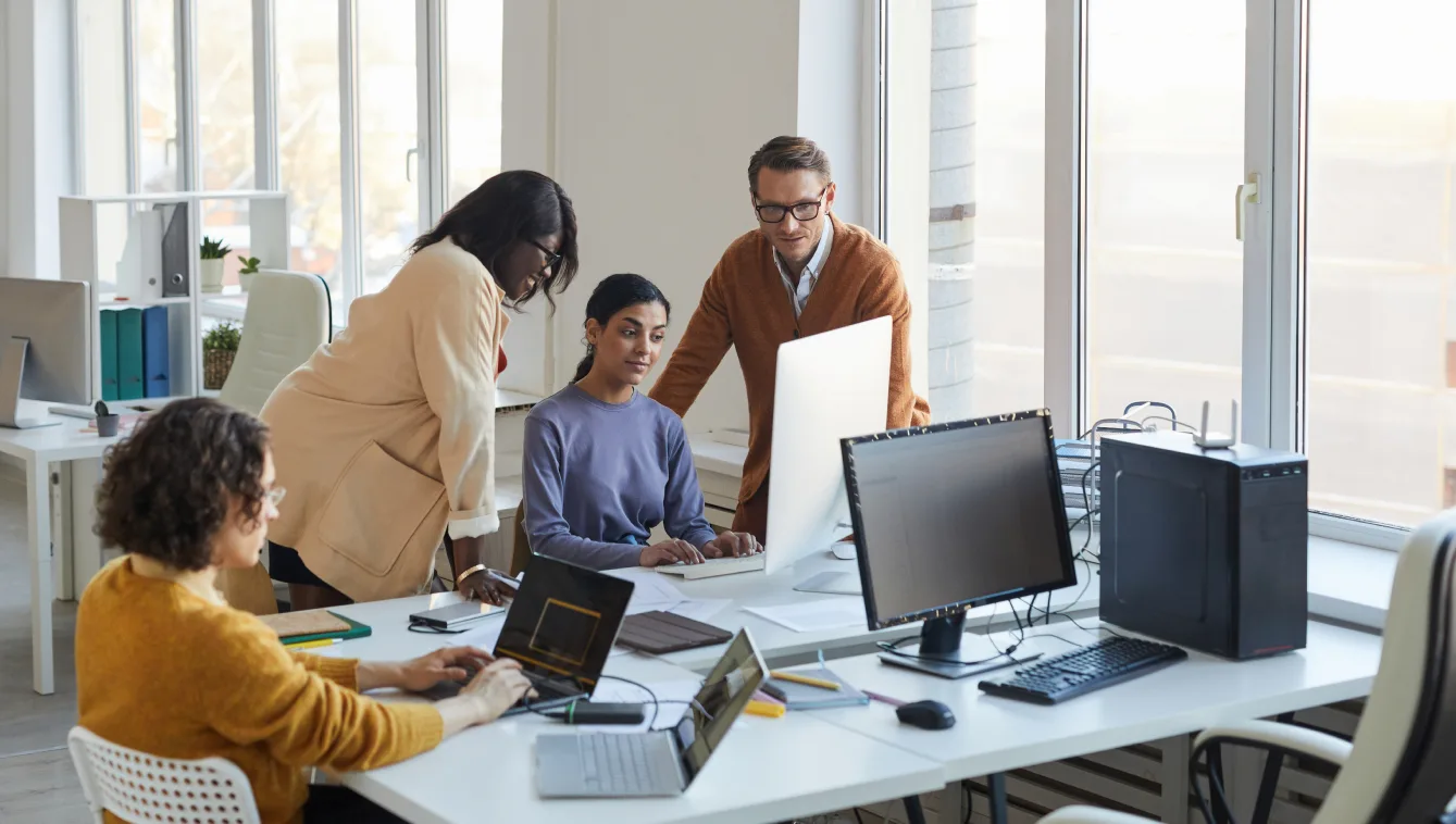 A team of professionals working together around a computer in an office.
